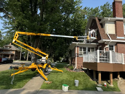 Boom lift working the upper gable of a brick two-story home